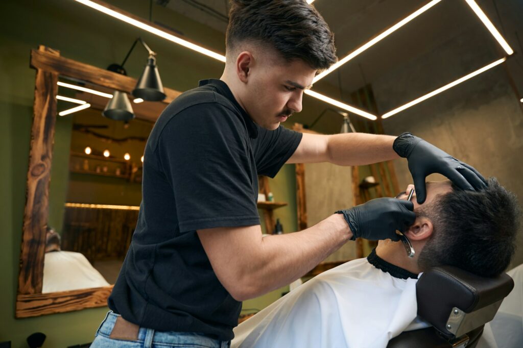 Barber trimming man's beard in barbershop