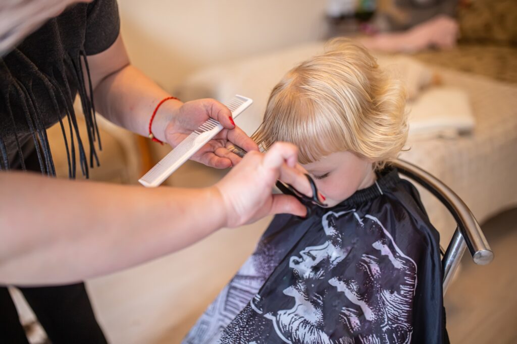 Hair salon at home. A hairdresser combs a child's hair in a beauty salon. Little girl getting a
